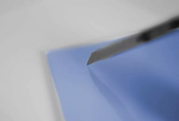 Cutter coupant feuille bleue sur surface blanche.