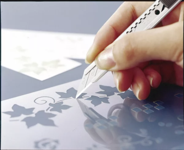 Main découpant pochoir de feuilles au cutter
