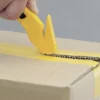 Main utilisant un cutter jaune sur carton